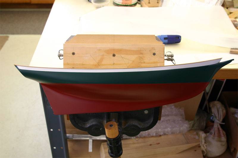 A photo of the replica model boat being built, the model is freshly painted and clamped onto the work bench before the custom transfer decals are applied.