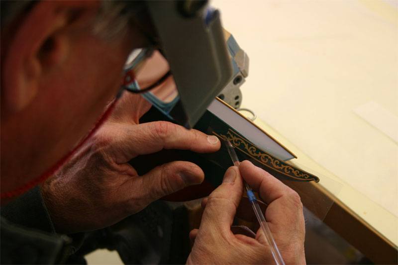 The model boat maker is using a burnishing tool to rub across the surface of the transfer to ensure smooth application.