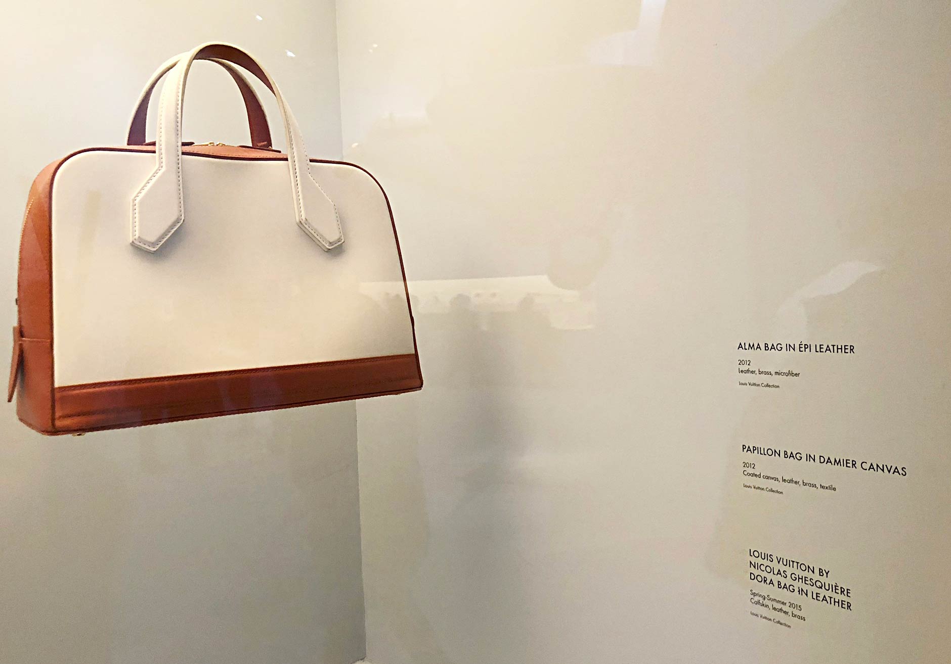 Louis Vuitton - Volez, Voguez, Voyagez exhibit, New York, NY. A leather, brass and microfiber handbag with cream-colored leather and light-auburn bottom and sides. Custom dry transfers are applied to the wall and used as descriptions for the piece.