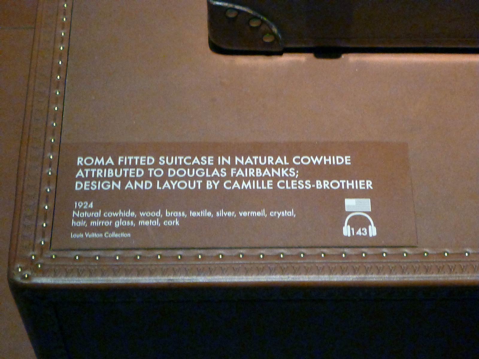 Louis Vuitton - Volez, Voguez, Voyagez exhibit, New York, NY. Custom dry transfer applied to leather placard reading, "ROMA FITTED SUITCASE IN NATURAL COWHIDE ATTRIBUTED TO DOUGLAS FAIRBANKS; DESIGN AND LAYOUT BY CAMILLE CLESS-BROTHIER".